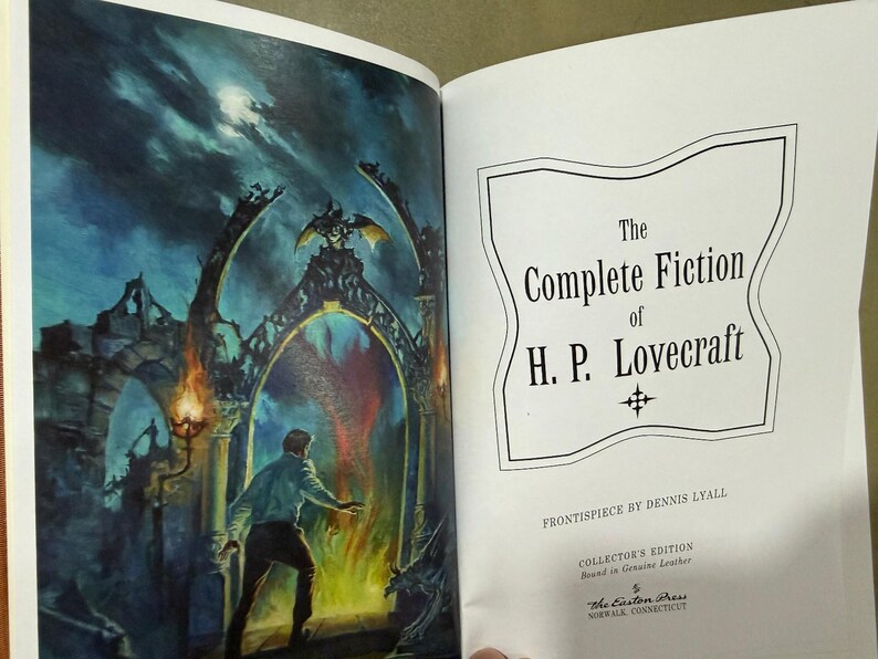 Puede incluir: Un libro abierto con una ilustraci&oacute;n en color y texto. La p&aacute;gina izquierda muestra a un hombre frente a un portal de fuego. La p&aacute;gina derecha muestra el t&iacute;tulo "The Complete Fiction of H.P. Lovecraft" en un marco decorativo. Es una edici&oacute;n de coleccionista.