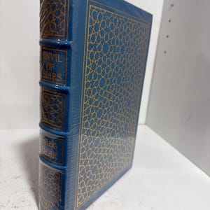May include: A hardcover book titled "Anvil of Stars" by Greg Bear. The book is wrapped in blue plastic and features a gold geometric pattern on the cover. The spine displays the title and author's name in gold lettering.