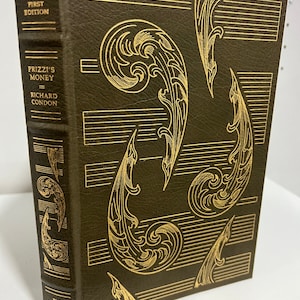Puede incluir: Un libro encuadernado en cuero verde con letras doradas y un diseño dorado en la portada. El título es "Prizzi's Money" de Richard Condon. El libro es una primera edición firmada y forma parte de The Franklin Library.