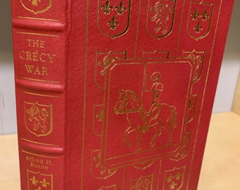 Puede incluir: Un libro de tapa dura rojo con letras doradas e ilustraciones. El título es "The Crecy War" de Alfred H. Burne.