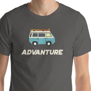 May include: A dark grey t-shirt featuring a vintage blue and white van with surfboards on the roof. The text "ADVANTURE" is printed in white below the van.