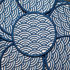 以下が含まれることがあります： 波模様の青い刺繍が施された丸いパッチのセット。パッチは円形に配置されています。