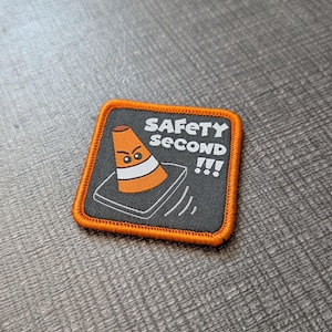 May include: Square patch with an orange border and the words "SAFETY SECOND !!!". The patch features an orange traffic cone with an angry face. The cone is on a gray background.
