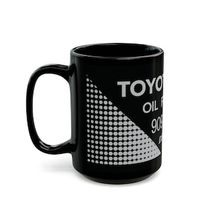 Könnte beinhalten: Schwarze Keramik-Kaffeetasse mit einer weißen Grafik eines Toyota-Ölfilters mit Teilenummer. Die Grafik hat ein schwarz-weißes Punktmuster.