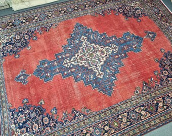 May include: A vintage Persian rug with a red background and a blue and white floral pattern in the center. The rug has a border of intricate floral designs in shades of blue, green, and cream.