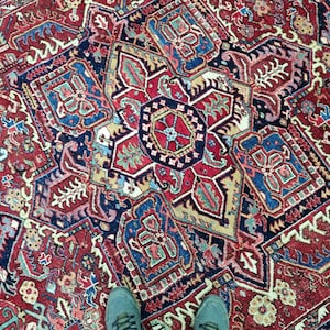 May include: A red, blue, and cream colored rug with a geometric pattern. The rug has a central medallion with a starburst design.