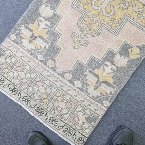 Puede incluir: Una alfombra de color rosa y gris con un dise&ntilde;o geom&eacute;trico. La alfombra tiene un borde de flecos.