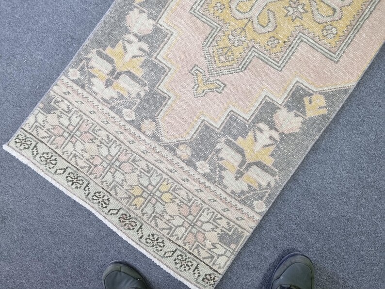 Puede incluir: Una alfombra de color rosa y gris con un dise&ntilde;o geom&eacute;trico. La alfombra tiene un borde de flecos.
