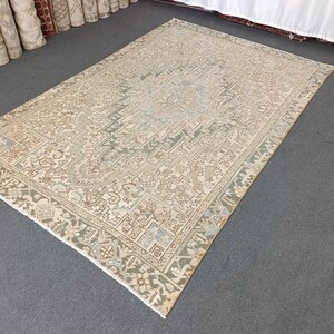 May include: A rectangular area rug with an intricate, faded design in shades of beige, light blue, and brown. The rug features a central pattern surrounded by a detailed border. The rug is placed on a gray surface.