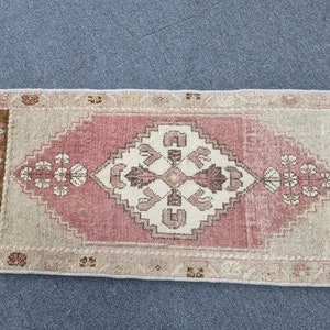 May include: A pink and beige runner rug with a white geometric pattern in the center. The rug has a fringe border.