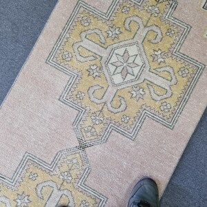 Puede incluir: Una alfombra de color rosa claro y amarillo con un dise&ntilde;o geom&eacute;trico. La alfombra tiene un aspecto descolorido y est&aacute; hecha de un material suave y tejido.