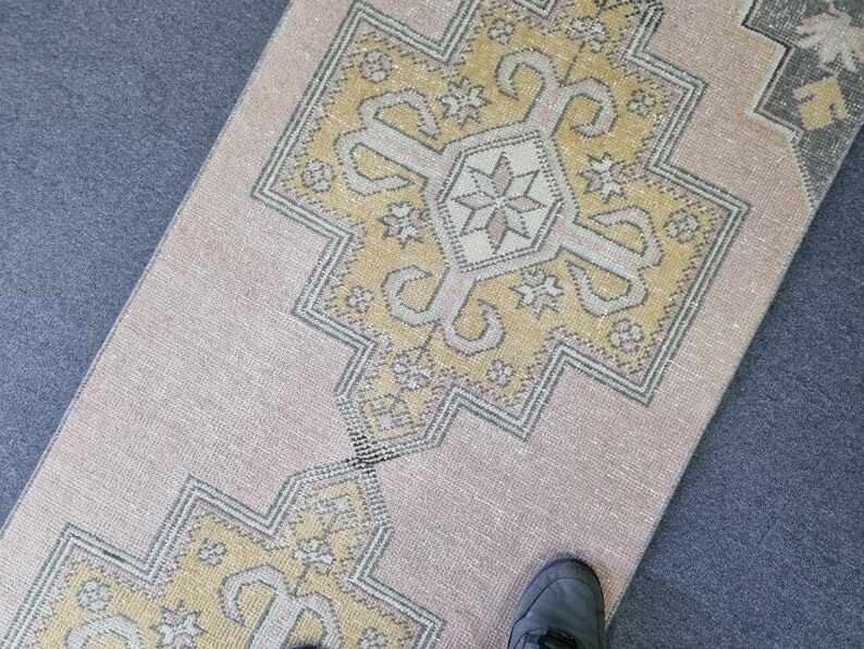 Puede incluir: Una alfombra de color rosa claro y amarillo con un dise&ntilde;o geom&eacute;trico. La alfombra tiene un aspecto descolorido y est&aacute; hecha de un material suave y tejido.