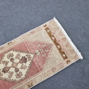 May include: A pink and beige runner rug with a geometric pattern and fringe on the edges.