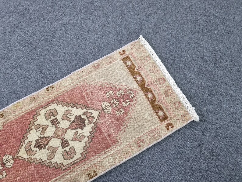 May include: A pink and beige runner rug with a geometric pattern and fringe on the edges.