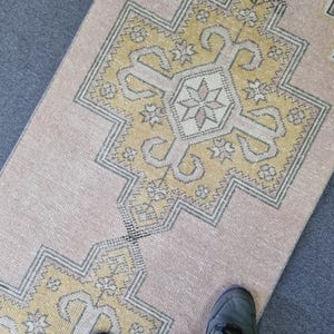 Puede incluir: Una alfombra de color rosa claro y amarillo con un dise&ntilde;o geom&eacute;trico. La alfombra tiene un aspecto descolorido y est&aacute; hecha de un material suave y tejido.