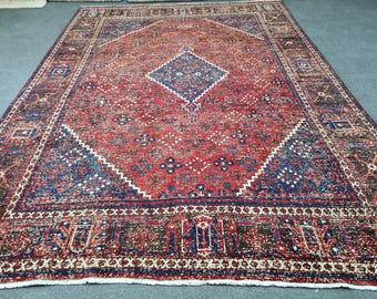 May include: A red, blue, and cream colored rug with a diamond pattern in the center. The rug has a fringe border.