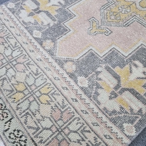 Puede incluir: Una alfombra vintage con un patr&oacute;n geom&eacute;trico en tonos rosa, gris y amarillo. La alfombra tiene un aspecto desgastado y est&aacute; hecha de un material suave y tejido.