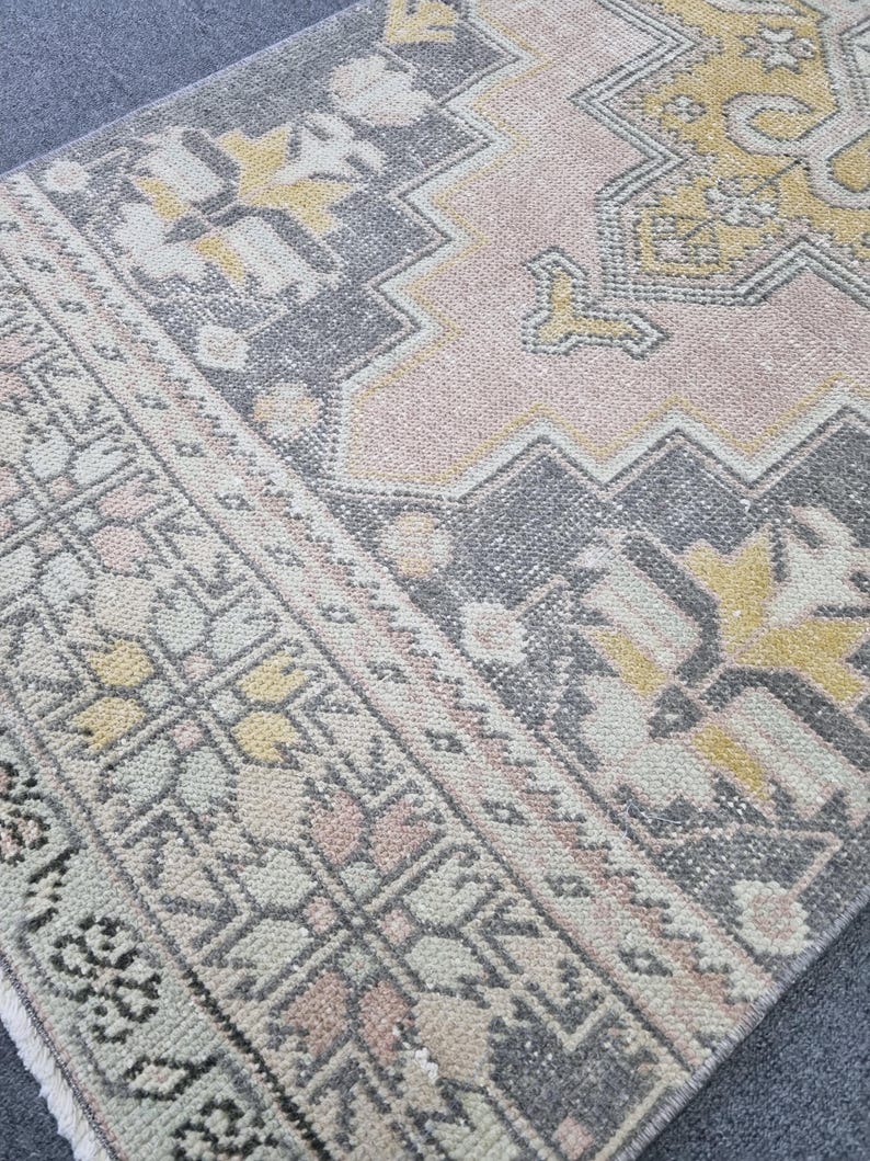 Puede incluir: Una alfombra vintage con un patr&oacute;n geom&eacute;trico en tonos rosa, gris y amarillo. La alfombra tiene un aspecto desgastado y est&aacute; hecha de un material suave y tejido.