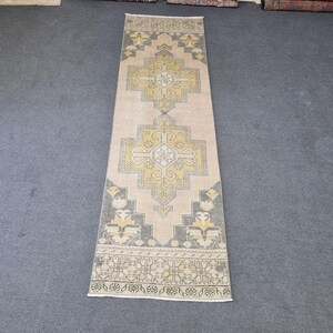 Puede incluir: Una alfombra rectangular larga con fondo crema y un patr&oacute;n geom&eacute;trico en tonos amarillos y grises. El patr&oacute;n presenta una forma de diamante central con cuatro diamantes m&aacute;s peque&ntilde;os dentro.