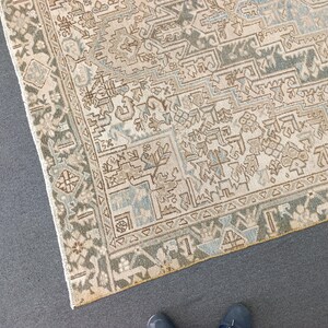 May include: An overhead shot of a beige and blue patterned rug with a detailed geometric design. The rug has a border with a darker green and beige pattern. The rug's design includes floral and geometric shapes.