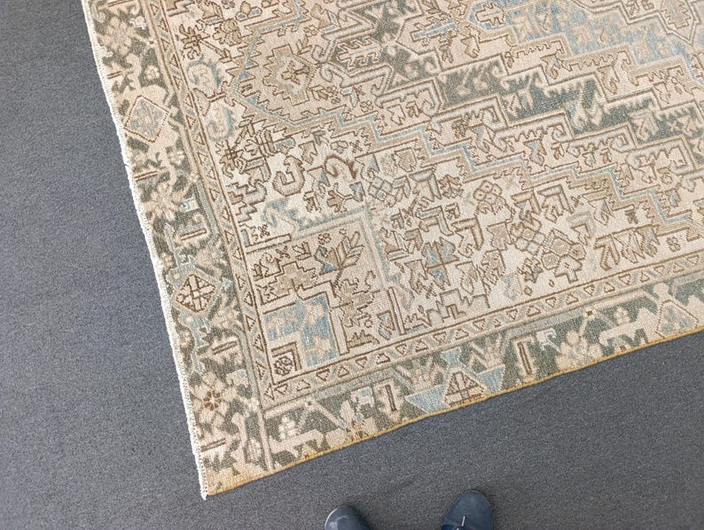 May include: An overhead shot of a beige and blue patterned rug with a detailed geometric design. The rug has a border with a darker green and beige pattern. The rug's design includes floral and geometric shapes.