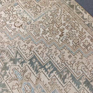 May include: Close-up of a beige and blue patterned rug. The rug features a geometric design with repeating shapes and a border. The colors include beige, light blue, and brown. The rug appears to be made of a woven material.