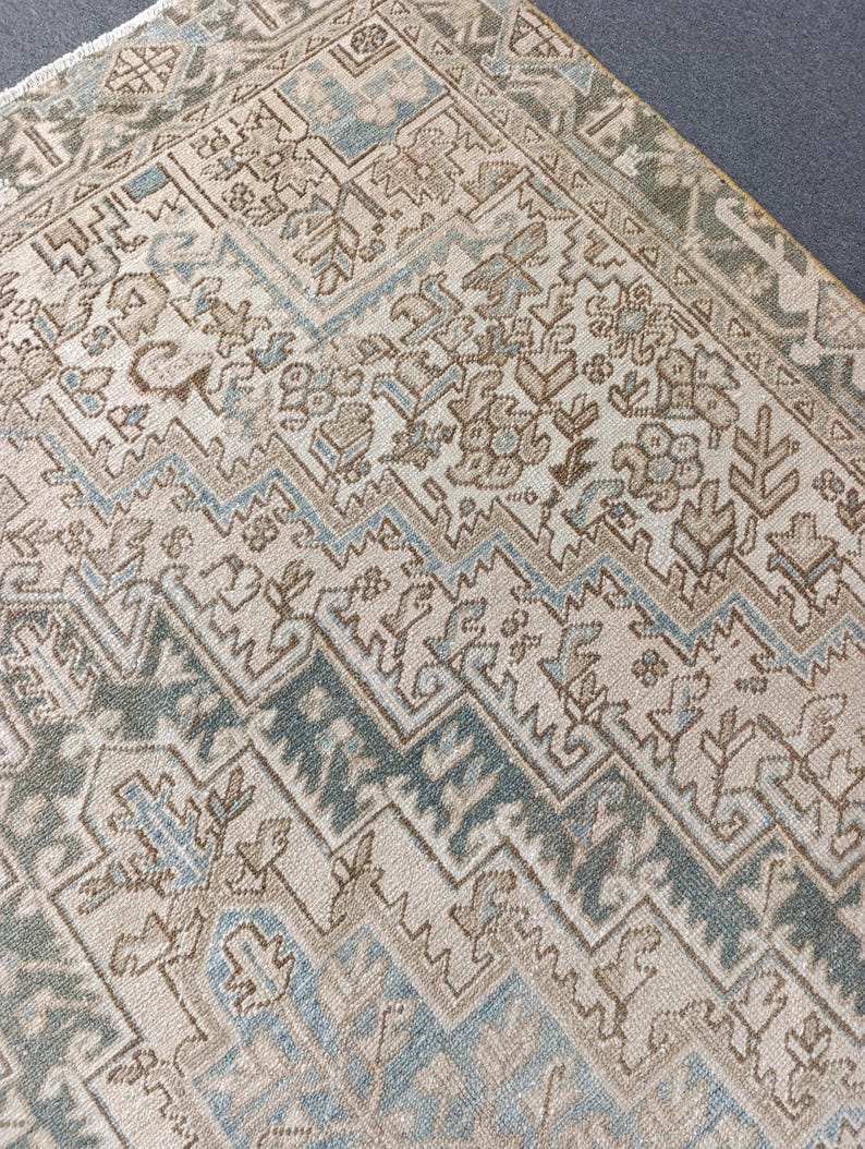 May include: Close-up of a beige and blue patterned rug. The rug features a geometric design with repeating shapes and a border. The colors include beige, light blue, and brown. The rug appears to be made of a woven material.
