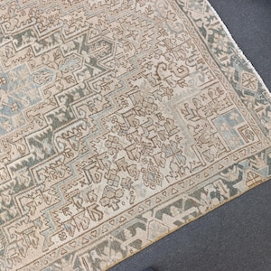 May include: An antique rug with a detailed geometric pattern in shades of beige, blue, and brown. The rug has a distressed look, with visible wear and tear, adding to its vintage charm. The border features a repeating triangular design.