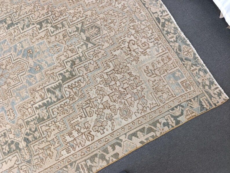 May include: An antique rug with a detailed geometric pattern in shades of beige, blue, and brown. The rug has a distressed look, with visible wear and tear, adding to its vintage charm. The border features a repeating triangular design.