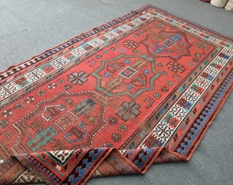 Könnte beinhalten: Ein rechteckiger, roter Vintage-Teppich mit komplizierten geometrischen Mustern in Blau-, Braun- und Weißtönen. Der Teppich hat ein zentrales Medaillon-Design und einen detaillierten Rand. Der Teppich ist teilweise aufgerollt und zeigt seine Unterseite.
