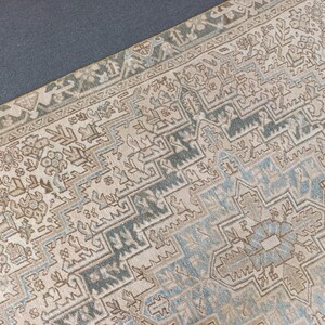 May include: Close-up of a beige and blue patterned rug. The rug features a detailed geometric design with a central medallion and border. The color palette includes beige, blue, and brown tones, creating a vintage aesthetic.