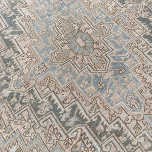May include: Close-up of a beige and blue patterned rug. The rug features a central geometric design with repeating patterns in shades of beige, blue, and brown. The rug has a distressed, vintage look.