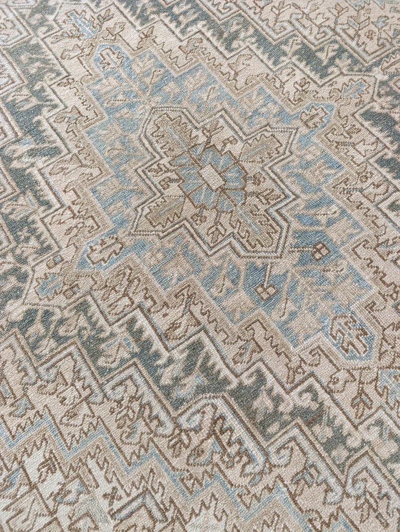 May include: Close-up of a beige and blue patterned rug. The rug features a central geometric design with repeating patterns in shades of beige, blue, and brown. The rug has a distressed, vintage look.