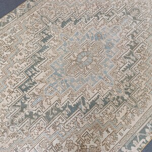 May include: A rectangular area rug with an intricate, geometric pattern. The rug features a central medallion in shades of blue and beige, surrounded by a border of teal and beige. The overall design is symmetrical and detailed, with a vintage aesthetic.