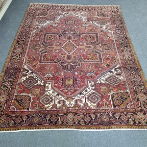 May include: A rectangular, patterned rug with a central medallion design. The rug features a complex geometric pattern in shades of red, brown, ivory, and gold. The border is a dark brown with repeating geometric shapes. The rug is likely made of wool.