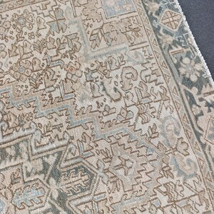 May include: Close-up of a section of a vintage rug with an intricate geometric pattern. The rug features a cream-colored background with detailed designs in shades of brown, blue, and green. The edges have a darker green border with a fringe.