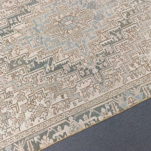 May include: An area rug with a detailed geometric pattern in shades of beige, blue, and brown. The rug features a central medallion design and a border with repeating motifs. The rug's texture appears soft and inviting, suitable for a living space.