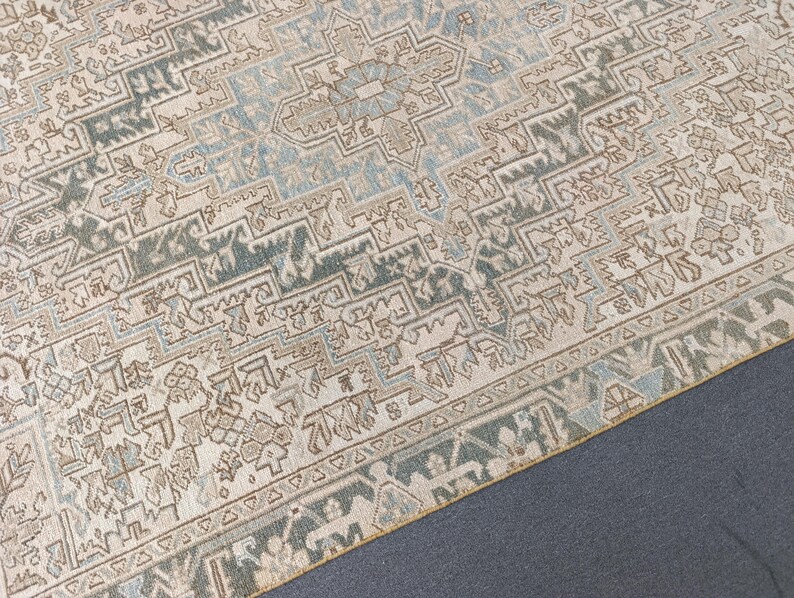 May include: An area rug with a detailed geometric pattern in shades of beige, blue, and brown. The rug features a central medallion design and a border with repeating motifs. The rug's texture appears soft and inviting, suitable for a living space.