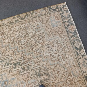 May include: An antique rug with a detailed geometric pattern in beige, blue, and green. The rug has a distressed look, with a faded appearance. The border features a darker green design. The rug is likely made of wool or a similar material.