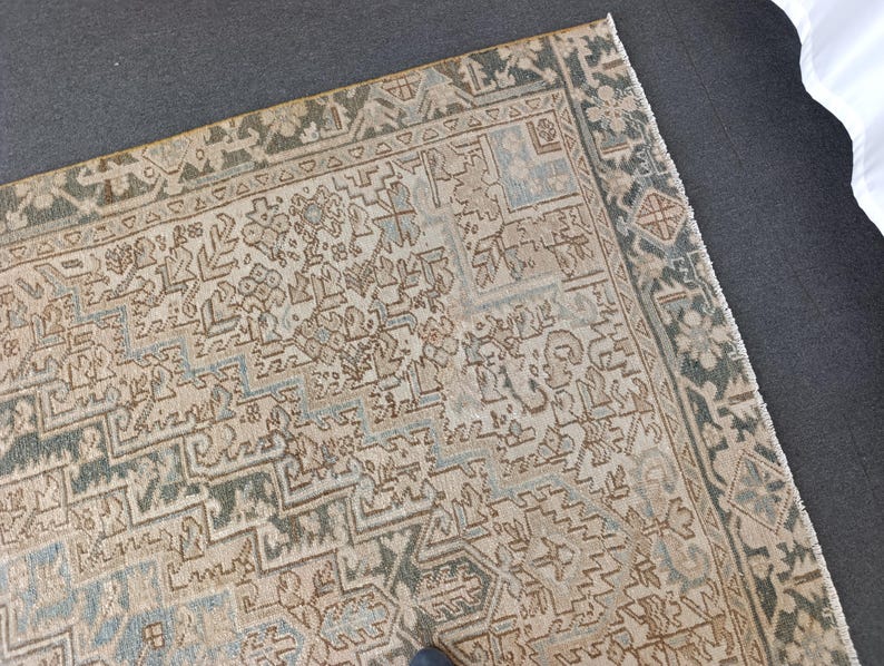 May include: An antique rug with a detailed geometric pattern in beige, blue, and green. The rug has a distressed look, with a faded appearance. The border features a darker green design. The rug is likely made of wool or a similar material.