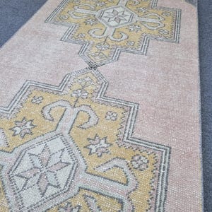 Puede incluir: Una alfombra de pasillo vintage con un patr&oacute;n geom&eacute;trico en tonos rosa, amarillo y gris. La alfombra tiene un aspecto desgastado y es perfecta para a&ntilde;adir un toque de estilo bohemio a cualquier habitaci&oacute;n.