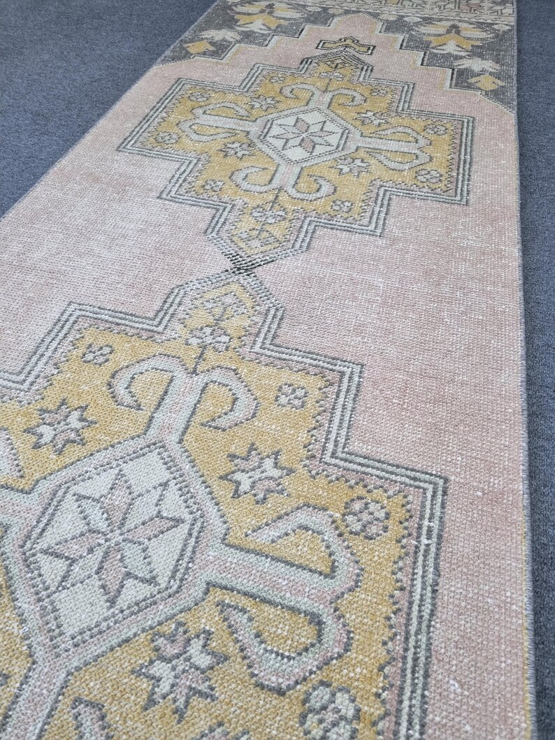 Puede incluir: Una alfombra de pasillo vintage con un patr&oacute;n geom&eacute;trico en tonos rosa, amarillo y gris. La alfombra tiene un aspecto desgastado y es perfecta para a&ntilde;adir un toque de estilo bohemio a cualquier habitaci&oacute;n.