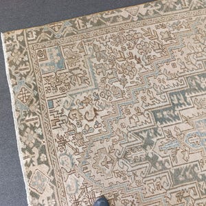 May include: A section of a vintage rug with an intricate geometric pattern. The rug features a beige background with accents of blue, brown, and green. The border has a detailed design in shades of green and beige, adding to the rug's antique aesthetic.