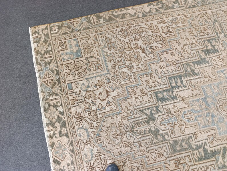 May include: A section of a vintage rug with an intricate geometric pattern. The rug features a beige background with accents of blue, brown, and green. The border has a detailed design in shades of green and beige, adding to the rug's antique aesthetic.