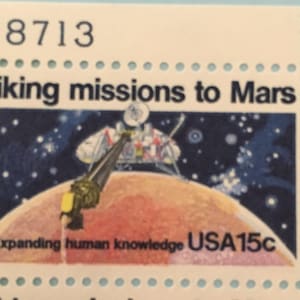 Puede incluir: Un sello postal estadounidense vintage que representa las misiones Viking a Marte. El sello muestra una nave espacial aterrizando en el planeta rojo con el texto "Viking missions to Mars" y "Expanding human knowledge USA15c".