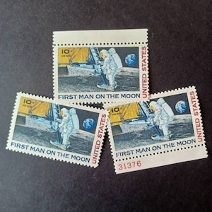 May include: Three vintage United States postage stamps featuring the "First Man on the Moon" design. Each stamp depicts an astronaut in a spacesuit standing on the moon's surface, with the Earth visible in the background. The stamps are in excellent condition and have a 10¢ airmail denomination.