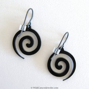 May include: A pair of black spiral earrings with silver wire and beads. The earrings are made of metal and have a simple, modern design.