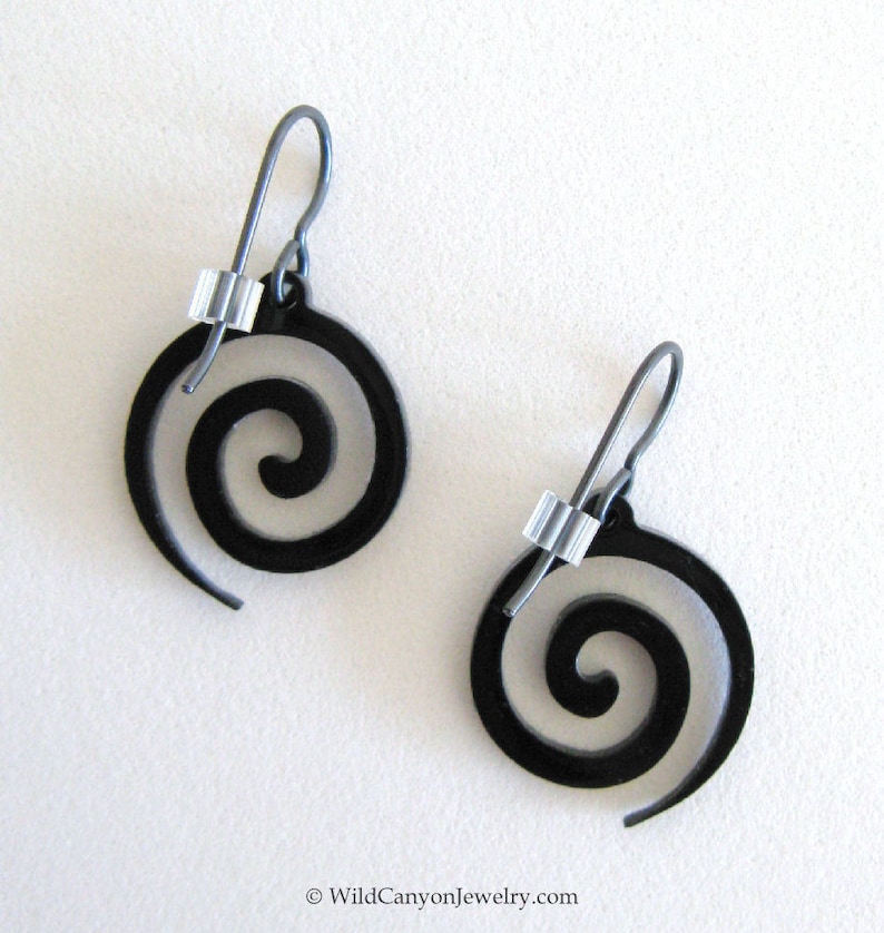 May include: A pair of black spiral earrings with silver wire and beads. The earrings are made of metal and have a simple, modern design.