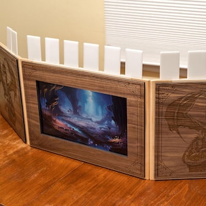 May include: A three-panel wooden game master screen with a fantasy landscape image in the center panel and a dragon design on each side panel. The screen has white dividers that can be adjusted to create different levels of privacy.