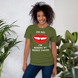 Pode incluir: Uma pessoa vestindo uma camiseta verde com um gráfico branco de uma boca com um dente faltando. O texto na camiseta diz "Oh não! Estou sem meu dente do meio!"